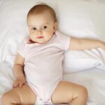 Portrait of cute nice little baby girl lying on pillow in bed. From above.