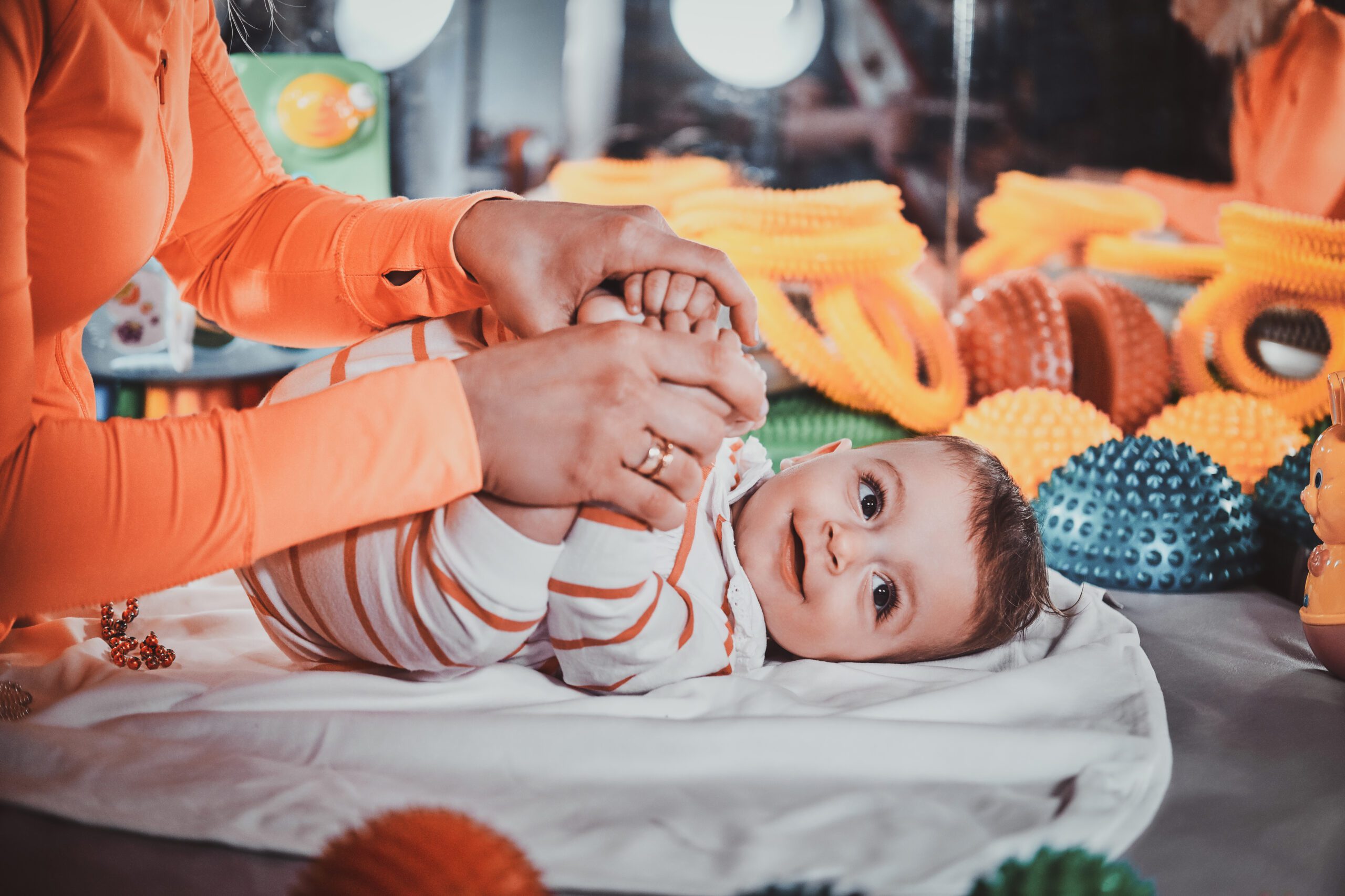 Happy smiling cute baby is lying on the special table surrounded by ortopedic toys