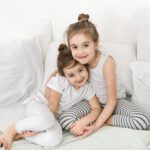 Two cute little sister girls cuddle on the bed in the bedroom.