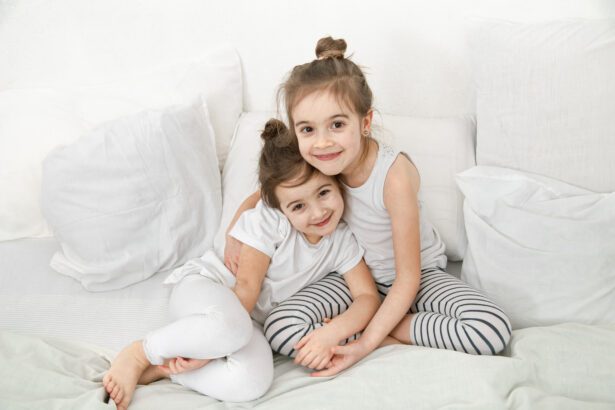 Two cute little sister girls cuddle on the bed in the bedroom.