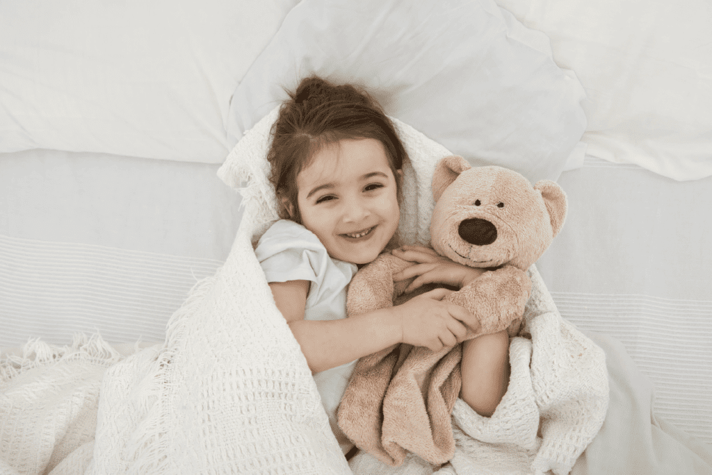 A child in soft pajamas resting in bed with a teddy bear