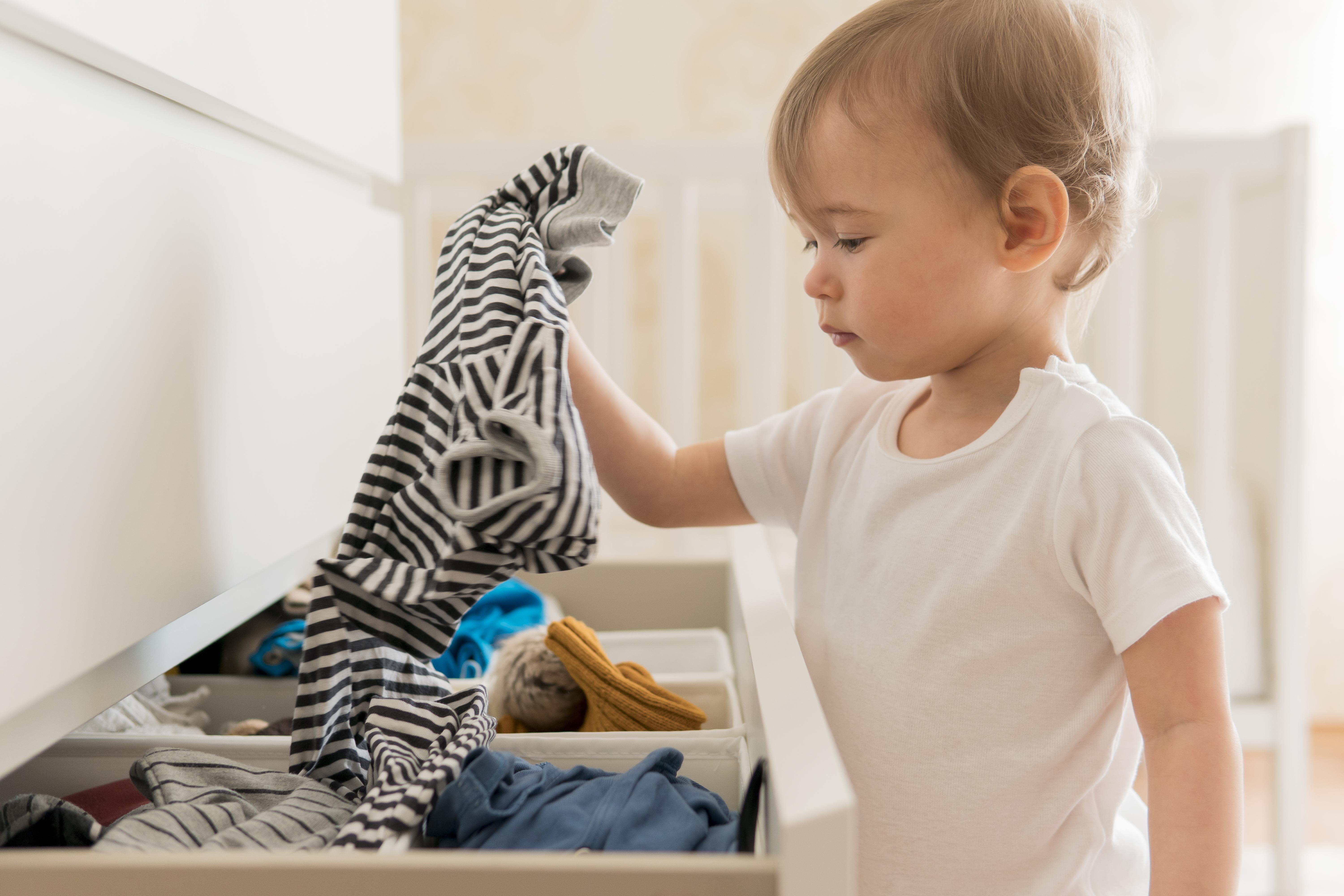 A young child selecting pajamas from a drawer