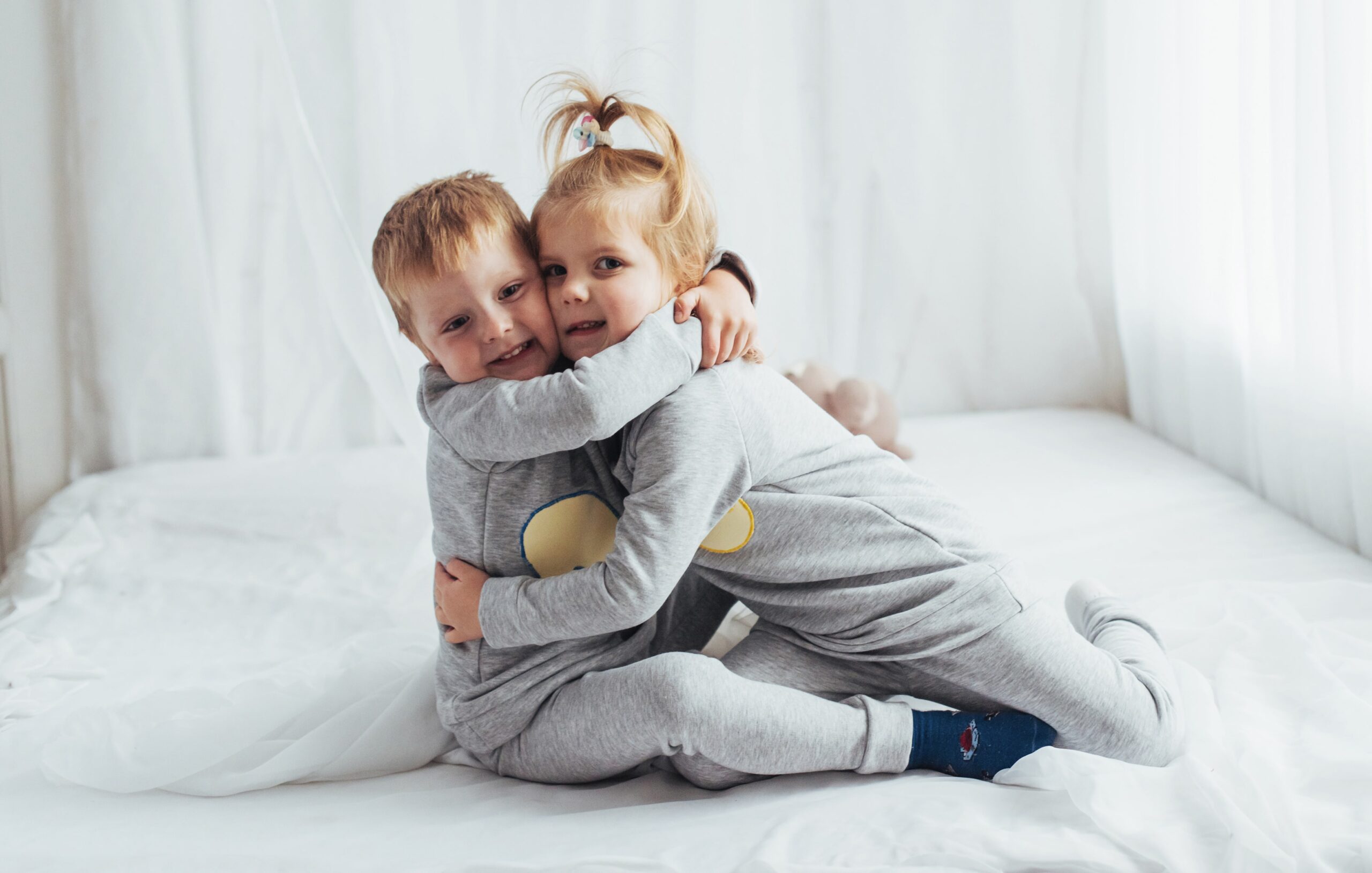 Two siblings, in matching PJs, giving each other a playful hug